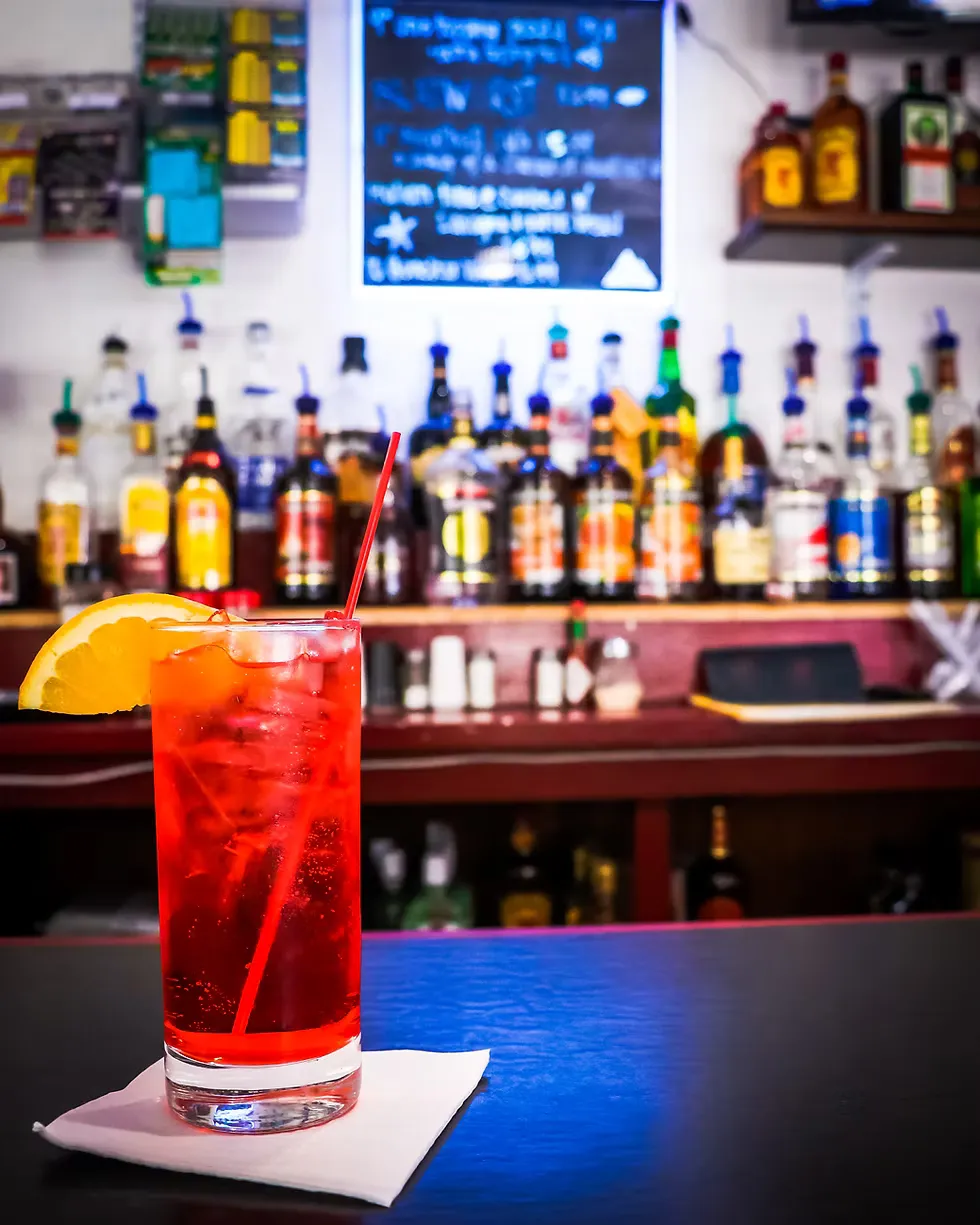 A red cocktail with an orange slice on the bar at Coolahan's Pub, with liquor bottles behind it