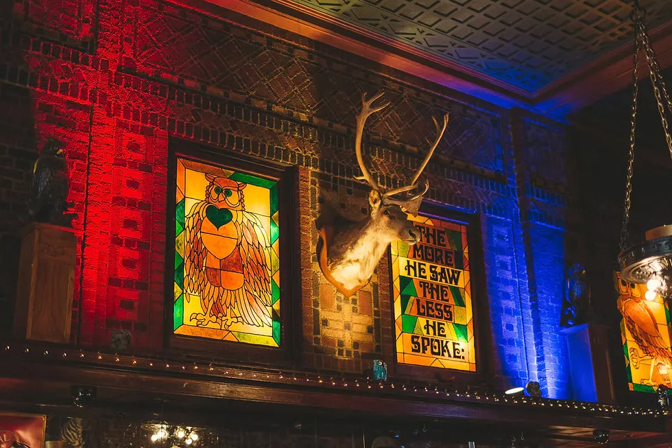 Stained glass owl windows and a mounted deer head above the bar at The Owl Bar